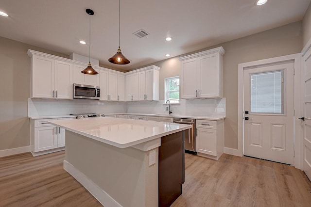 kitchen with stainless steel appliances, a kitchen island, sink, decorative light fixtures, and white cabinetry