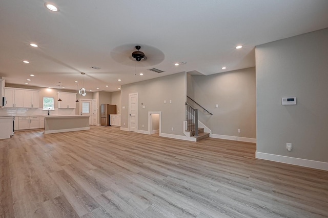 unfurnished living room featuring light hardwood / wood-style floors, ceiling fan, and sink