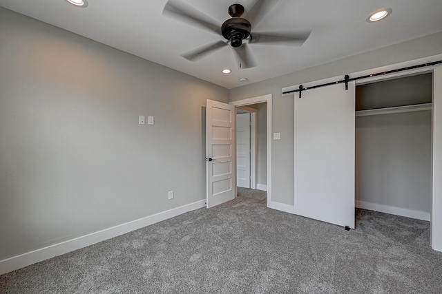 unfurnished bedroom with ceiling fan, a barn door, carpet floors, and a closet