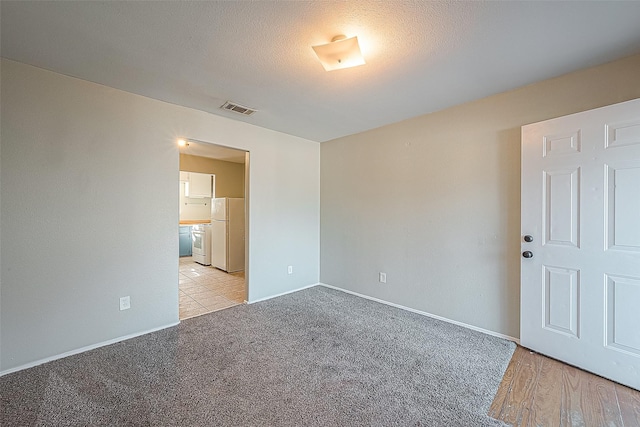 spare room with light colored carpet and a textured ceiling