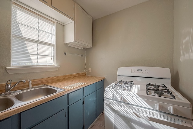 kitchen with blue cabinetry, light tile patterned floors, sink, and white range with gas cooktop