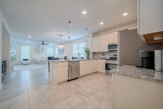 kitchen with kitchen peninsula, appliances with stainless steel finishes, light stone countertops, ceiling fan, and hanging light fixtures