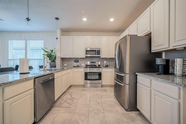 kitchen featuring light stone counters, stainless steel appliances, sink, decorative light fixtures, and white cabinets