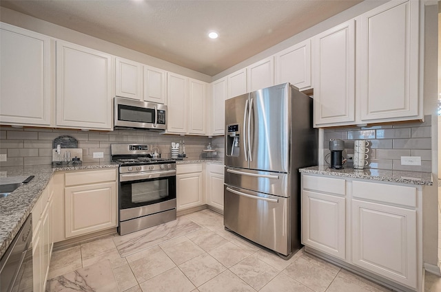 kitchen featuring white cabinets, decorative backsplash, stainless steel appliances, and light stone countertops