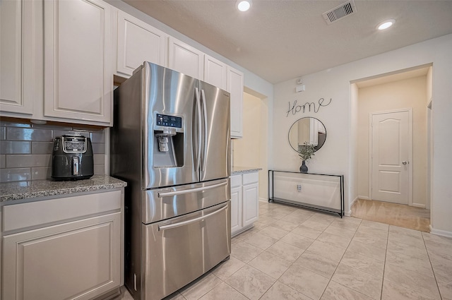 kitchen with decorative backsplash, stainless steel fridge, white cabinetry, and light stone countertops