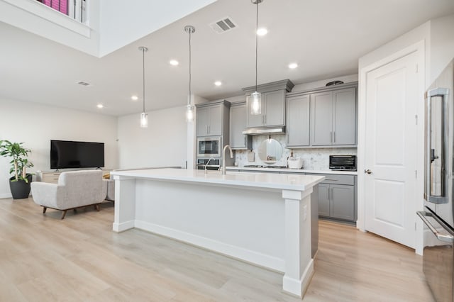 kitchen featuring gray cabinets, appliances with stainless steel finishes, decorative backsplash, a center island with sink, and decorative light fixtures