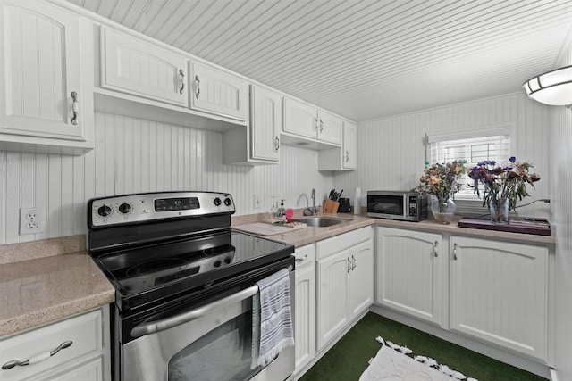 kitchen featuring appliances with stainless steel finishes, white cabinetry, wood walls, and sink