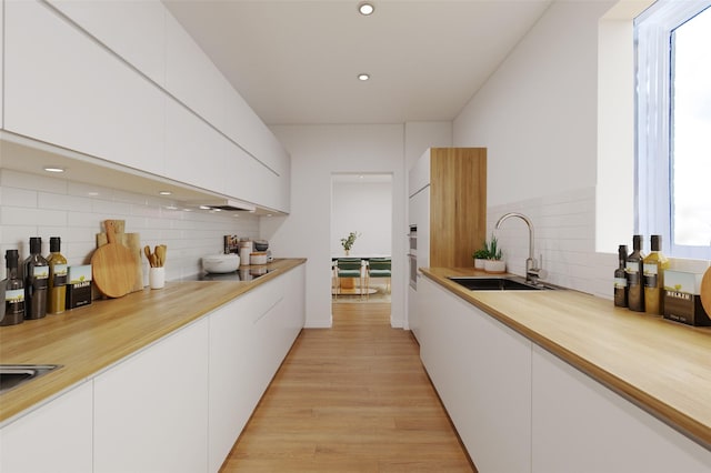 kitchen with white cabinets, light wood-type flooring, backsplash, and sink