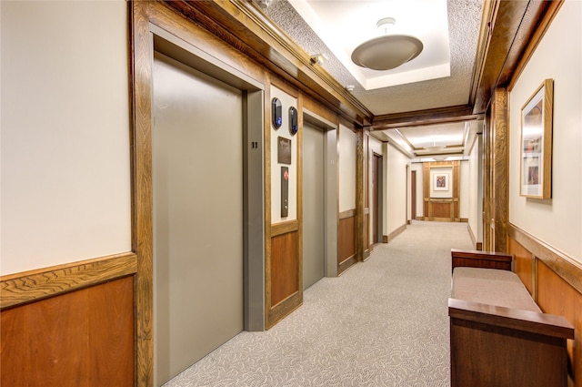 corridor featuring elevator, a raised ceiling, wood walls, crown molding, and light carpet