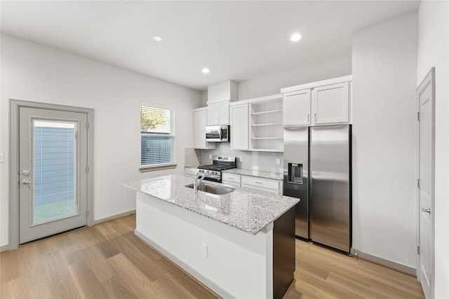 kitchen with white cabinetry, backsplash, stainless steel appliances, light stone countertops, and a center island with sink