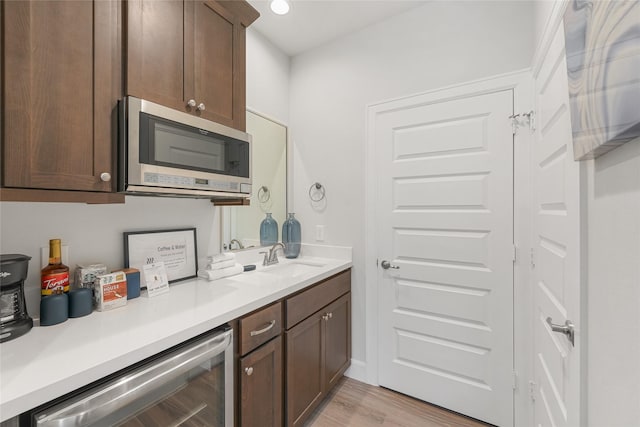 kitchen featuring sink, beverage cooler, dark brown cabinets, and light wood-type flooring