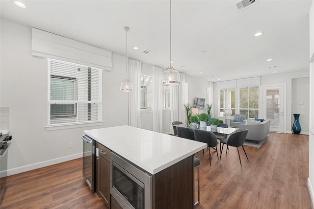 kitchen featuring dark hardwood / wood-style flooring, dark brown cabinets, stainless steel microwave, beverage cooler, and hanging light fixtures