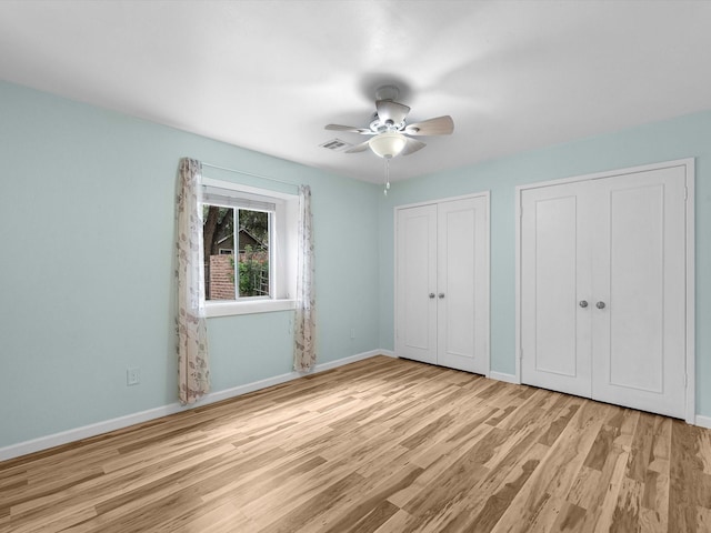 unfurnished bedroom with ceiling fan, multiple closets, and light hardwood / wood-style flooring