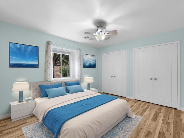 bedroom with ceiling fan, light hardwood / wood-style floors, and multiple closets