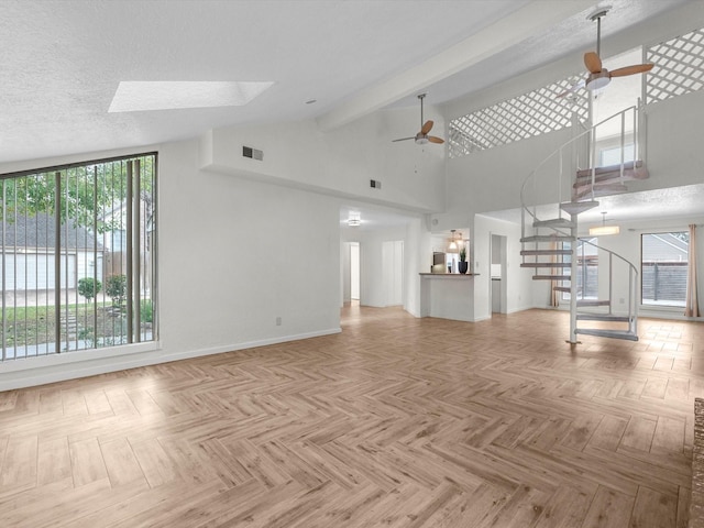 unfurnished living room with ceiling fan, light parquet flooring, and a skylight