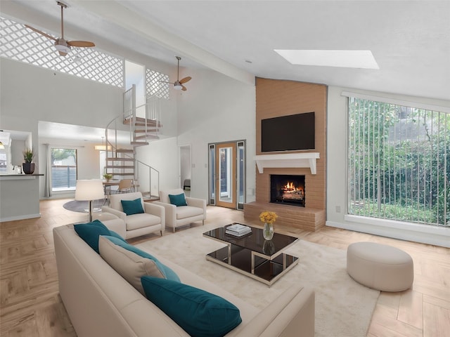 living room featuring ceiling fan, light parquet flooring, a brick fireplace, a high ceiling, and a skylight