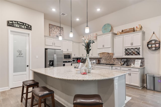 kitchen featuring white cabinets, pendant lighting, stainless steel appliances, and an island with sink