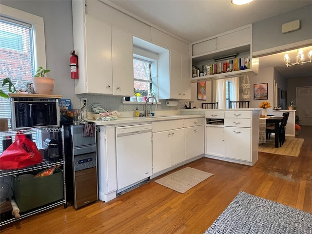 kitchen with dishwasher, white cabinets, sink, light hardwood / wood-style floors, and kitchen peninsula