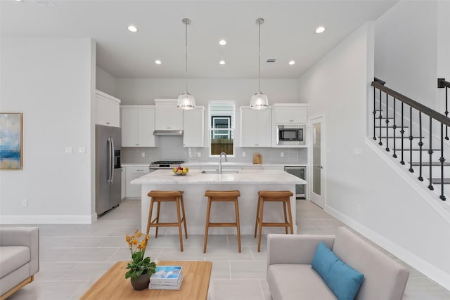 kitchen with white cabinetry, sink, stainless steel appliances, a kitchen breakfast bar, and a center island with sink