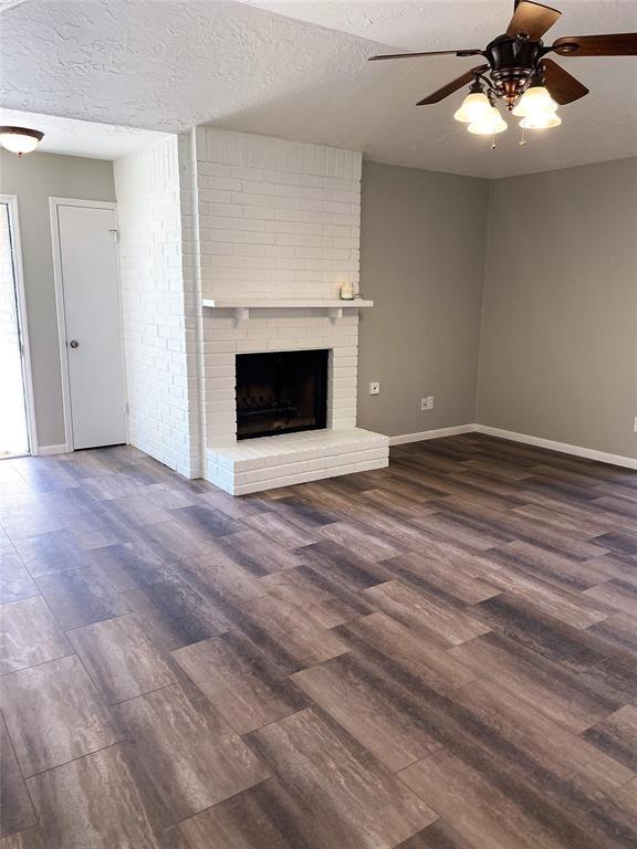 unfurnished living room featuring dark wood-type flooring, ceiling fan, a brick fireplace, and a textured ceiling