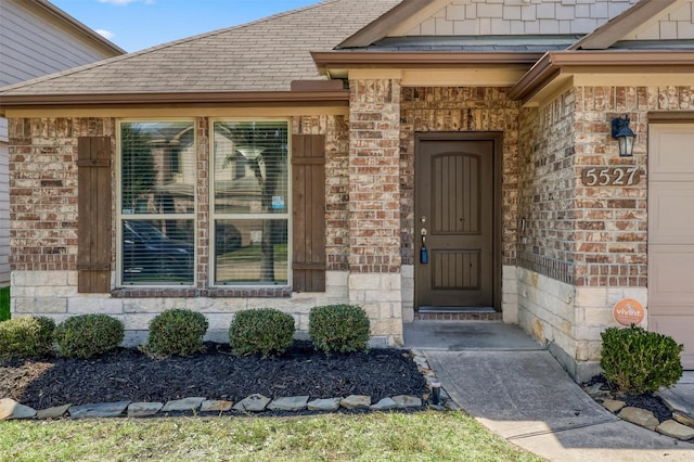 entrance to property with a shingled roof, brick siding, and an attached garage