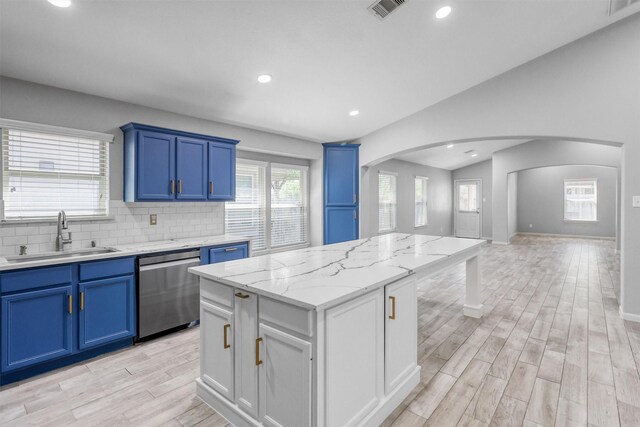 kitchen featuring light stone countertops, a center island, sink, stainless steel dishwasher, and vaulted ceiling