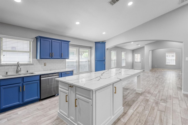 kitchen with light stone counters, arched walkways, stainless steel dishwasher, a kitchen island, and a sink