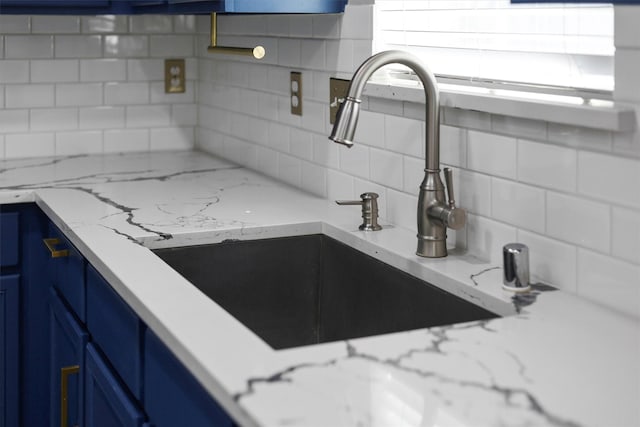 kitchen with backsplash, light stone counters, sink, and blue cabinets