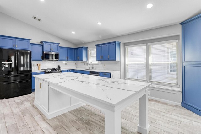 kitchen featuring light stone countertops, appliances with stainless steel finishes, lofted ceiling, a kitchen island, and light wood-type flooring