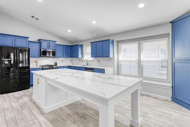 kitchen with lofted ceiling, stainless steel appliances, a kitchen island, decorative backsplash, and light stone countertops