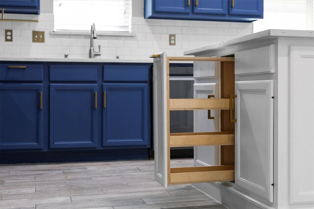 kitchen featuring blue cabinetry, decorative backsplash, sink, and light hardwood / wood-style floors