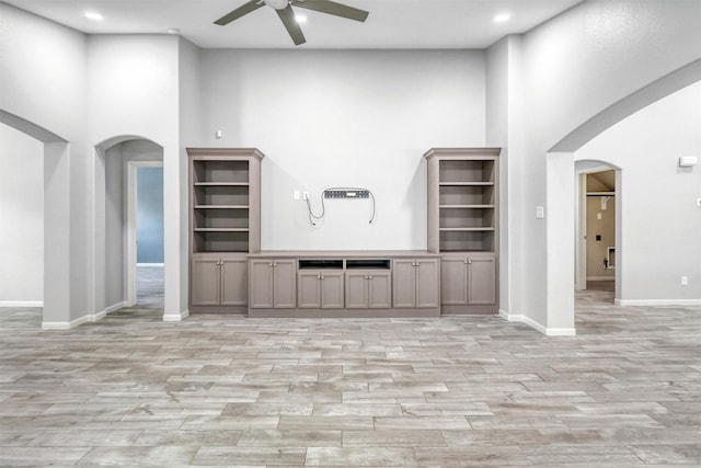 unfurnished living room featuring ceiling fan and a high ceiling