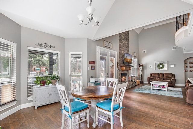 dining room with a stone fireplace, dark wood-type flooring, high vaulted ceiling, and a chandelier