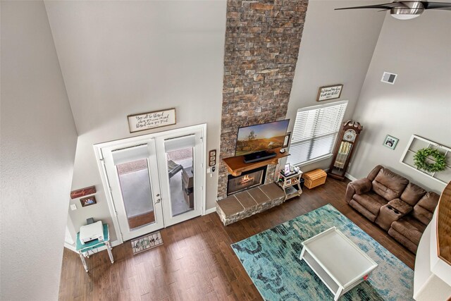 living room with dark wood-type flooring, french doors, ceiling fan, a towering ceiling, and a fireplace