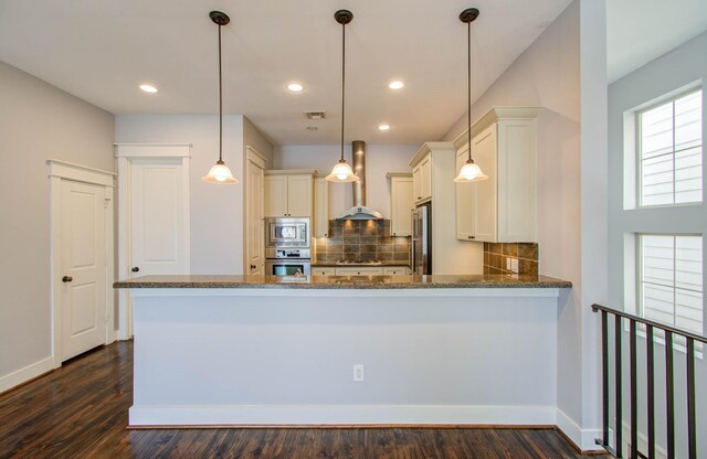 kitchen featuring wall chimney exhaust hood, appliances with stainless steel finishes, tasteful backsplash, decorative light fixtures, and kitchen peninsula