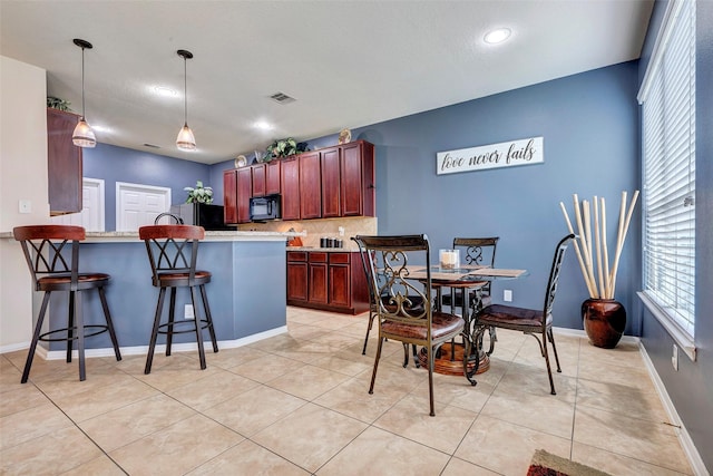 kitchen with pendant lighting, backsplash, black appliances, kitchen peninsula, and a breakfast bar area