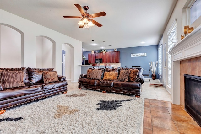 tiled living room with ceiling fan and a fireplace