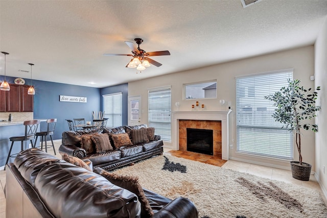 living room featuring a tiled fireplace, ceiling fan, light tile patterned floors, and a textured ceiling