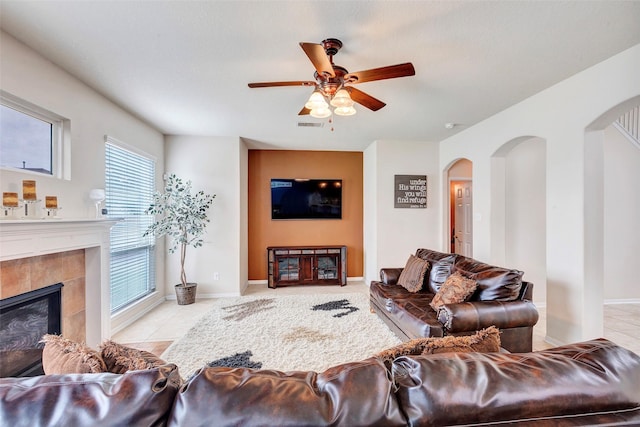 living room featuring ceiling fan, a fireplace, and light tile patterned floors