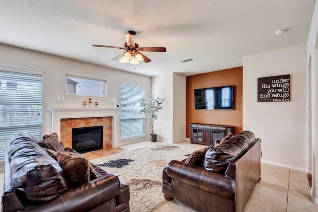 tiled living room featuring a tile fireplace, a textured ceiling, and ceiling fan