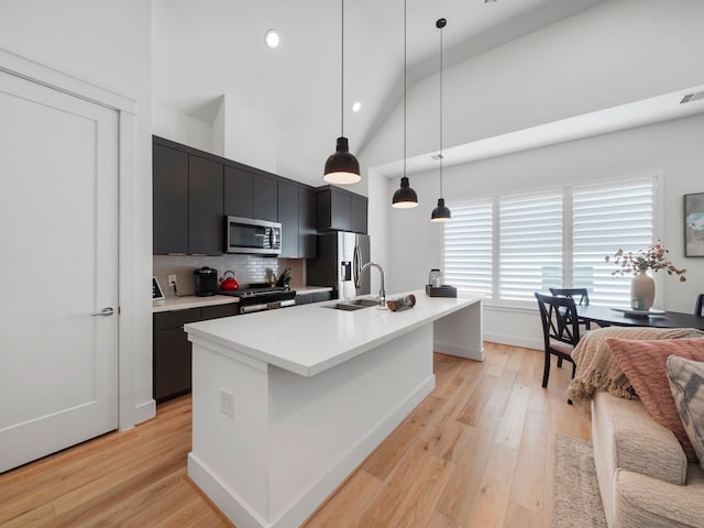 kitchen featuring sink, light wood-type flooring, appliances with stainless steel finishes, pendant lighting, and a kitchen island with sink