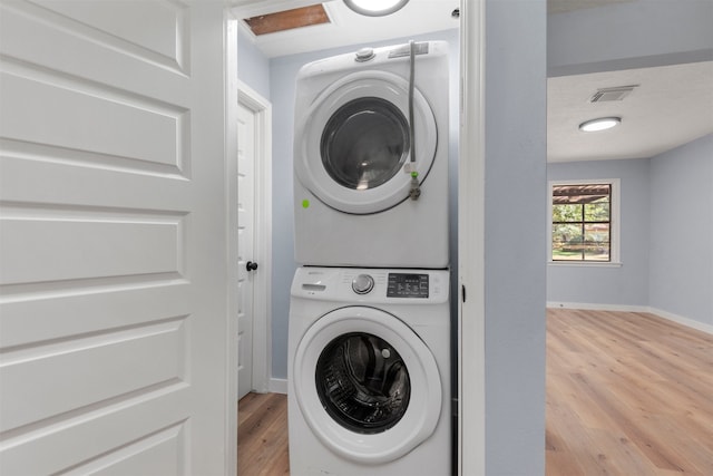 clothes washing area featuring light hardwood / wood-style floors and stacked washer / dryer