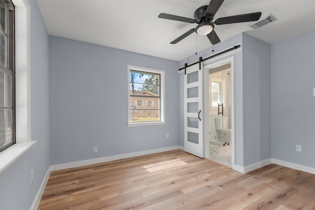 spare room featuring ceiling fan, a barn door, and light wood-type flooring