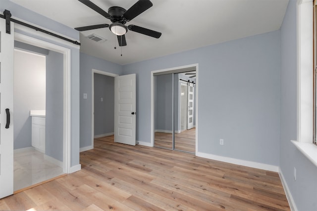 unfurnished bedroom featuring a barn door, ceiling fan, a closet, and light wood-type flooring