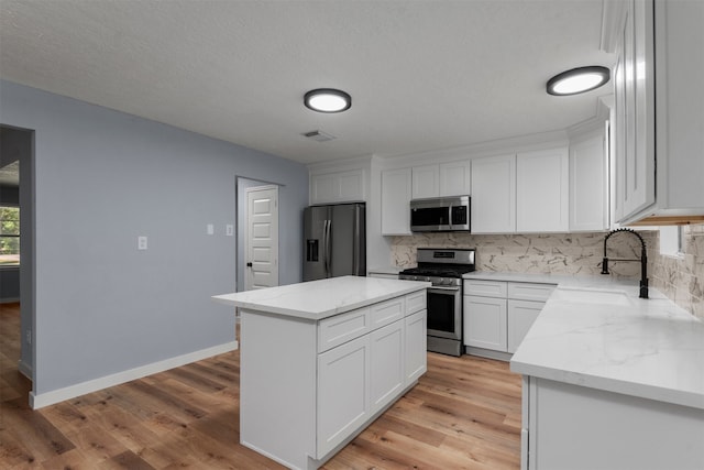 kitchen with a center island, sink, decorative backsplash, appliances with stainless steel finishes, and white cabinetry