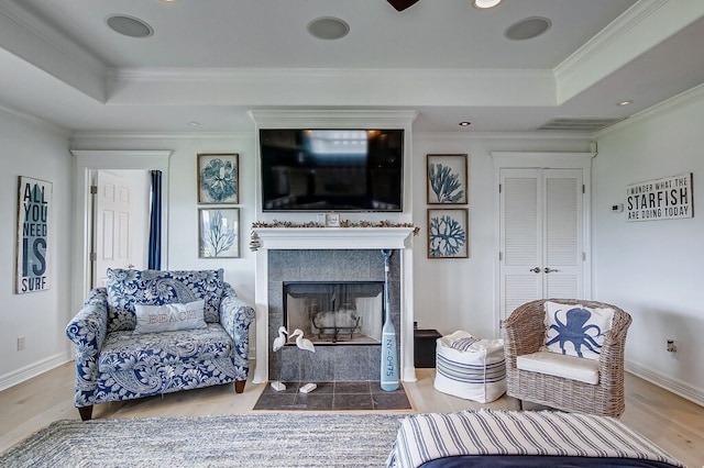 living room with a raised ceiling, a tiled fireplace, hardwood / wood-style flooring, and ornamental molding