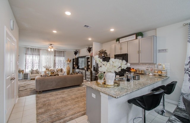 kitchen featuring kitchen peninsula, a kitchen breakfast bar, gray cabinetry, ceiling fan, and light tile patterned floors