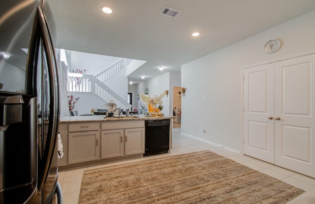 kitchen with stainless steel fridge, light tile patterned floors, light stone counters, and black dishwasher