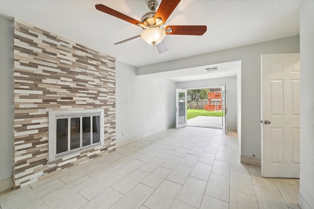 unfurnished living room featuring ceiling fan and a tiled fireplace