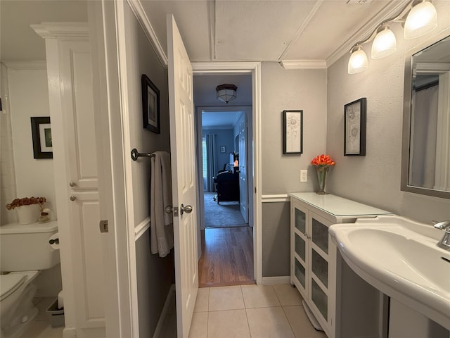 bathroom with toilet, tile patterned floors, ornamental molding, and sink